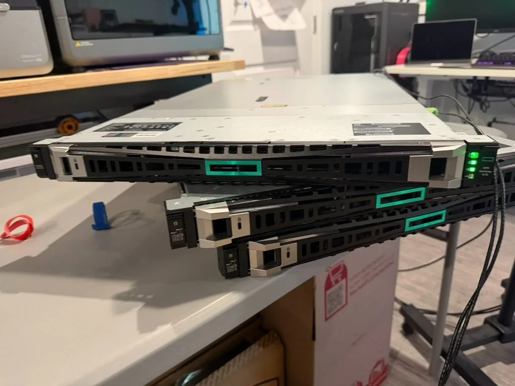 Three 1U HPE servers stacked on the bench, bezels on, powered up.